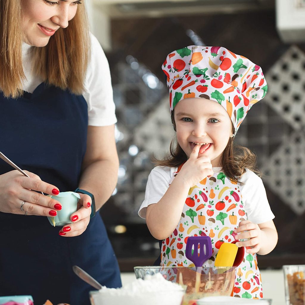 Young Girl Wearing Vegatable Print Apron And Chef Hat Included In RiseBrite Ultimate Real Kids Cooking Set