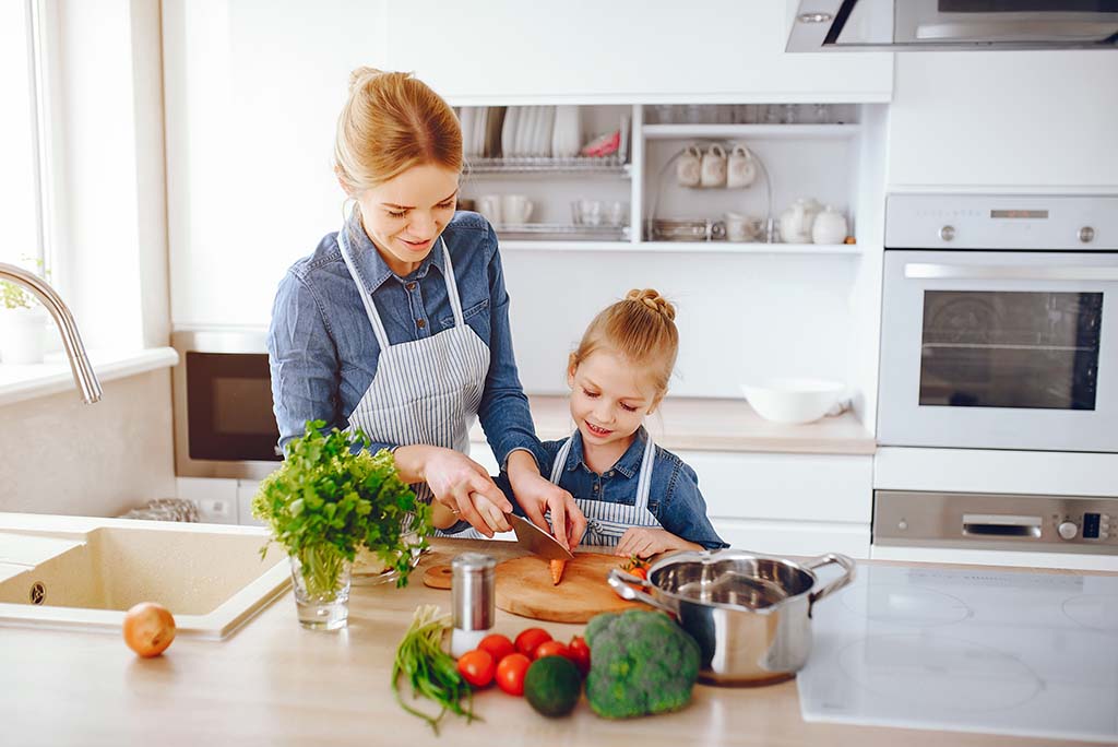 Young Mother And Daughter Cutting Vegetables In The Kitchen