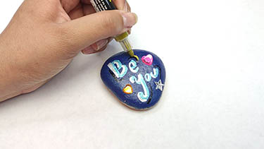 Kindness Rock Painting Tutorial Step 11: Use the metallic gold acrylic marker to highlight the detailed lines.